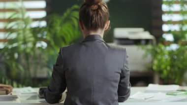 Sürdürülebilir iş yeri. Modern yeşil ofiste meditasyon yapan gri takım elbiseli modern iş kadınının arkasından görüldü..