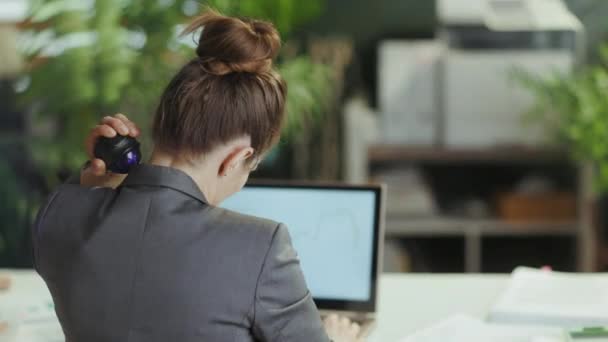 持続可能な職場 現代の緑のオフィスで灰色のビジネススーツの現代のビジネス女性の後ろから見た首にマッサージローラーを使用して — ストック動画