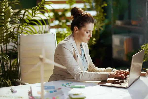 modern 40 years old accountant woman in a light business suit in modern green office with laptop.