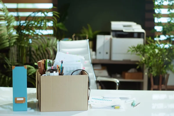 New job. desk in modern green office with personal belongings in cardboard box.