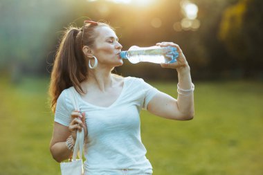 Yaz zamanı. Beyaz gömlekli, orta yaşlı, rahat bir kadın açık alanda su içiyor..