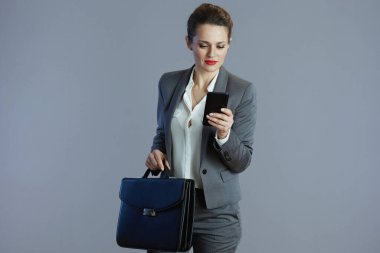 Gri takım elbiseli, akıllı telefonu ve gri çantasıyla şık, şık, küçük işletme sahibi kadın..