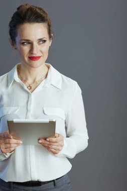 Kırk yaşında, beyaz bluzlu, tabletli, gri arka planda izole edilmiş bir iş kadını..