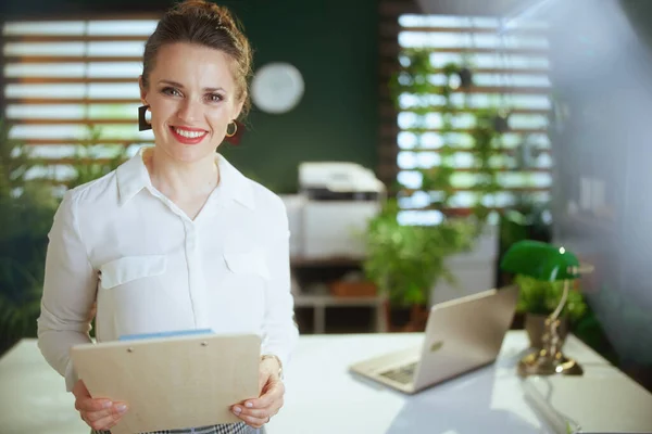 Time to move on. happy stylish woman real estate agent in modern green office in white blouse with clipboard.