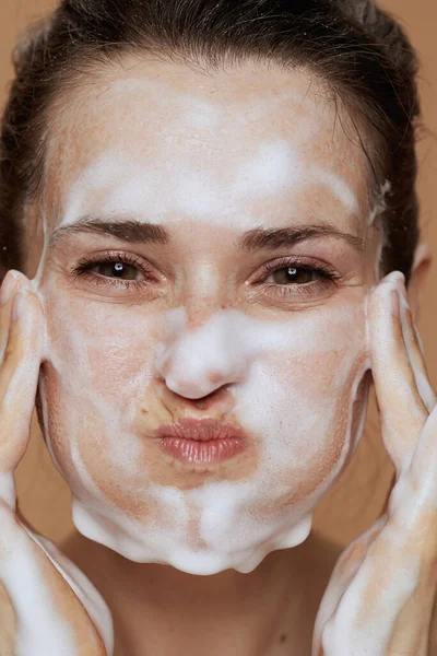 smiling young female with foaming facial cleanser washing face.