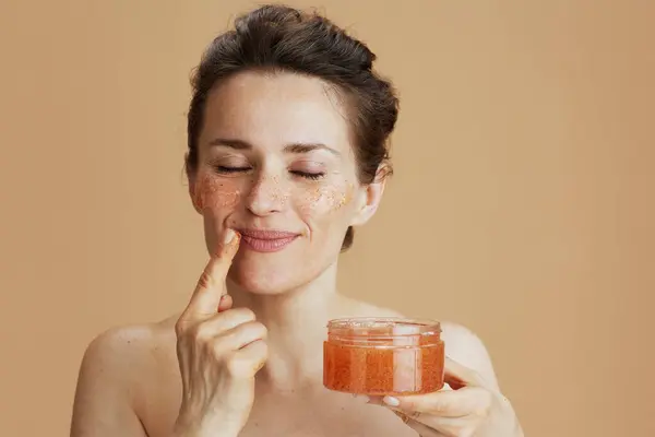 relaxed modern woman with face scrub isolated on beige.