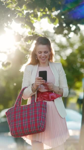 Zbliżenie Kobietę Różowej Sukience Białej Kurtce Mieście Smartfonem Czerwoną Torbą — Wideo stockowe