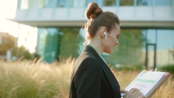 幸せな現代 ドキュメント フォルダ ワイヤレスヘッドフォン付きブラックジャケットのビジネス地区の古いビジネス女性 — ストック動画