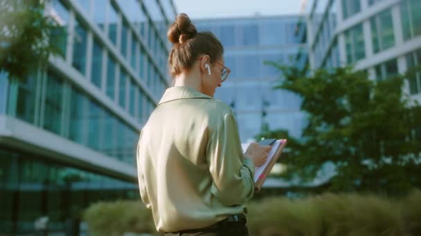 在商业中心附近工作的中年妇女身穿绿色衬衫 手持智能手机文件 从背后看到 — 图库视频影像