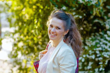 40 yaşında, pembe elbiseli ve kırmızı çantalı beyaz ceketli mutlu bir kadının portresi..