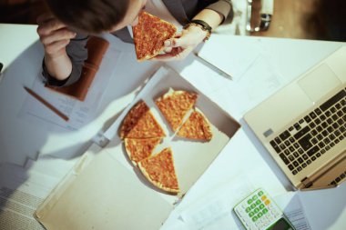 Sürdürülebilir iş yeri. Yeşil ofisteki pizza ve dizüstü bilgisayarlı kadın işçinin üst görüntüsü..