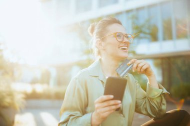 Yeşil bluzlu, gözlüklü, akıllı telefon kullanan 40 yıllık mutlu modern kadın işçi..