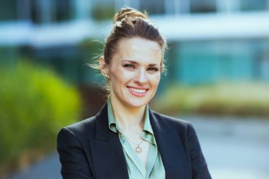 Ofis binasının yanındaki siyah ceketli mutlu kadın işçinin portresi..