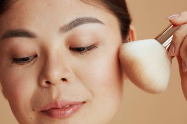 Bej arka planda makyaj fırçası olan genç bir kadın..