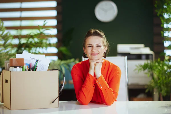 New job. happy modern woman worker in modern green office in red blouse with personal belongings in cardboard box.