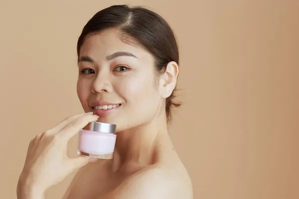 Moderno Asiático Fêmea Com Facial Creme Jar Contra Bege Fundo — Fotografia de Stock