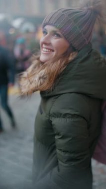 Gülümseyen 40 yaşındaki yeşil paltolu ve kahverengi şapkalı kadın şehirdeki kış fuarında.