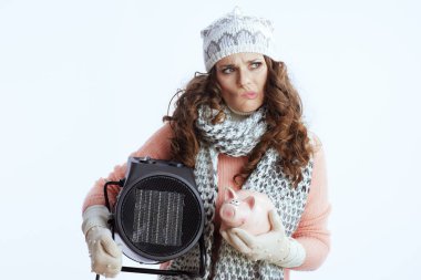 Merhaba kış. Süveter, eldiven, şapka ve eşarp giymiş şık bir kadın. Isıtıcı ve domuz kumbaralı beyaz arka planda..