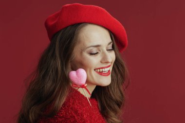 Happy Valentine. smiling trendy woman in red sweater and beret with heart on stick.