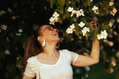 Yaz zamanı. Çiçek açan ağacın yanında gözlüklü, beyaz gömlekli mutlu bir bayan..