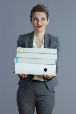 Gri arka planda klasörleri olan gri takım elbiseli modern kadın çalışanı vurguladı.