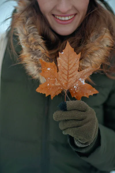 冬季带着手套和秋叶在城市公园外微笑的女性的衣服 — 图库照片