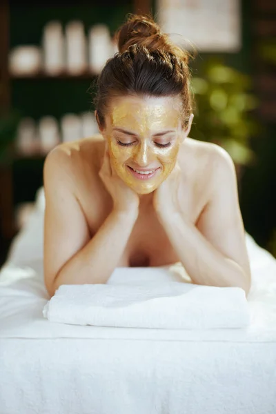 Healthcare time. happy modern female in spa salon with golden cosmetic mask on face laying on massage table.