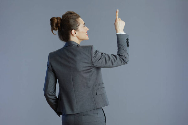 Seen from behind woman worker in grey suit pointing up isolated on grey.