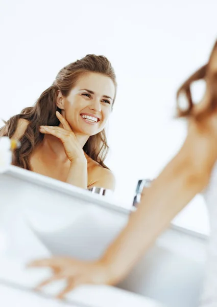 Happy woman looking in mirror in bathroom