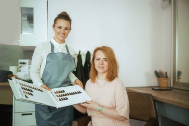 40 yaşında kadın kuaför. Saç rengi grafiği ve müşterisiyle modern saç stüdyosunda çalışıyor..