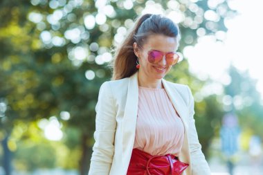 Mutlu, orta yaşlı, pembe elbiseli, beyaz ceketli, güneş gözlüklü bir kadın..