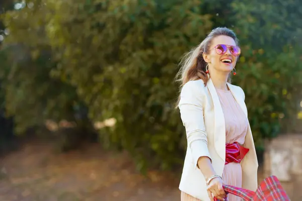 穿着粉红衣服 身穿白色夹克 头戴红包和太阳镜的现代女性微笑着走着 — 图库照片