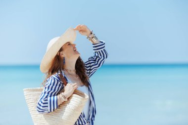Gülümseyen stil 40 yaşında bir kadın saman torbası ve hasır şapkayla sahilde eğleniyor..