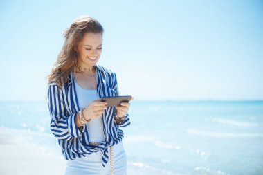 Deniz kıyısında akıllı telefonlu mutlu orta yaşlı bir kadın..