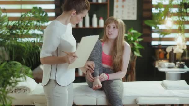 Gesundheitszeit Betroffene Massagetherapeutin Massageschrank Mit Klemmbrett Und Jugendliche Kundin Hört — Stockvideo