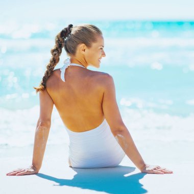 Deniz kenarında oturan ve üzerinde kopya yer arayan genç bir kadın. arka görünüm