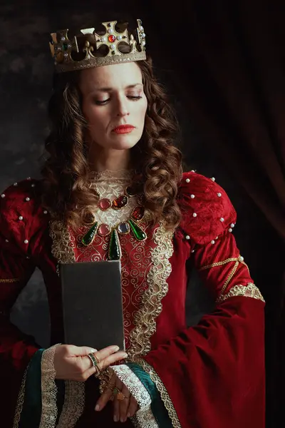 medieval queen in red dress with book and crown on dark gray background.