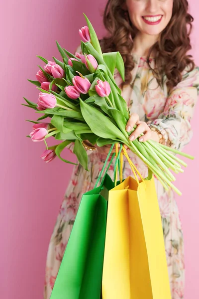 ピンクの背景に隔離されたチューリップブーケとショッピングバッグで花のドレスで笑顔の中年女性のクローズアップ — ストック写真