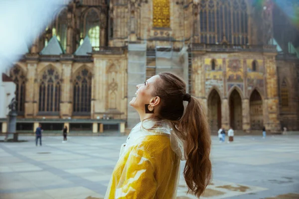 在布拉格 穿着黄色衬衫和雨衣的快乐的现代旅游妇女正在享受散步 — 图库照片