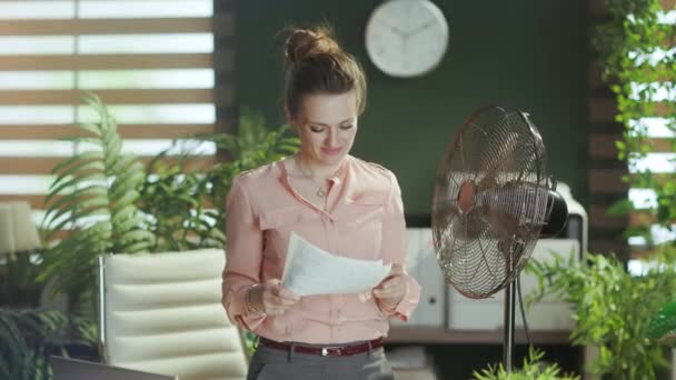 可持续工作场所 在现代绿色办公室工作的快乐的中年妇女 有文件和电扇 — 图库视频影像