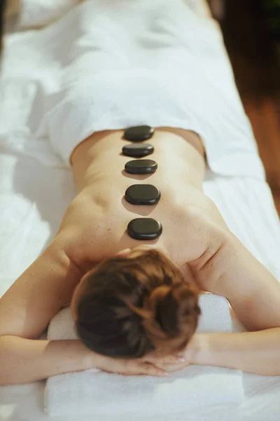 Healthcare time. relaxed modern middle aged woman in massage cabinet having hot stone massage and laying on massage table.