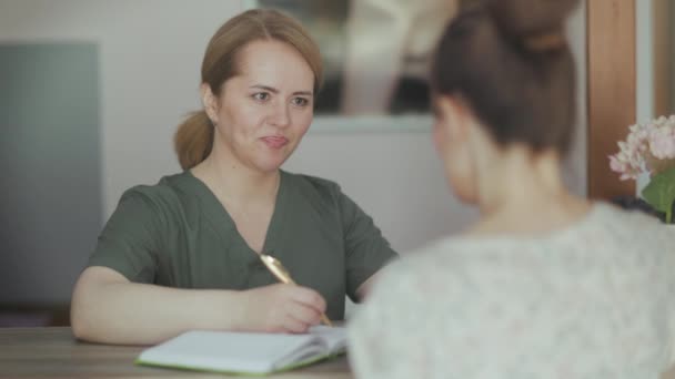 医療時間について 受付にクライアントとノートが付いているマッサージキャビネットのペンシブ女性マッサージ療法士 — ストック動画