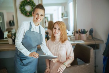 Modern güzellik stüdyosunda tableti ve müşterisi olan kadın kuaför..