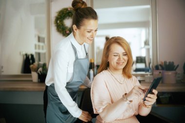 Modern güzellik salonunda akıllı telefonlu bir müşteriyle kadın kuaför..