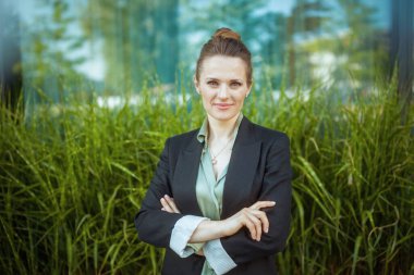 Mutlu modern kadın çalışanın portresi iş bölgesinde siyah ceketli ve kollarını kavuşturmuş..