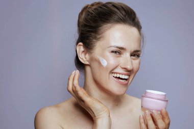 Mavi arka planda kozmetik krema kavanozuyla gülümseyen genç bir kadının portresi.