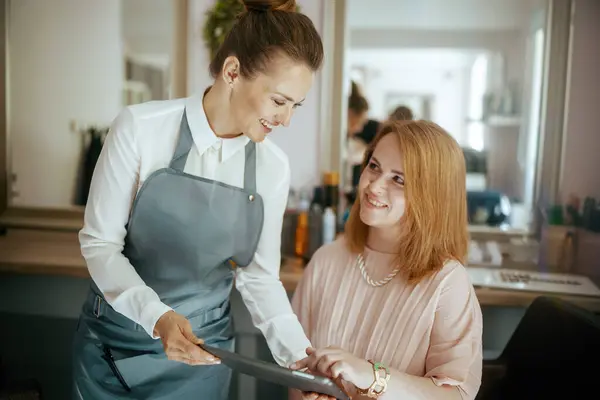 Modern saç stüdyosunda tableti ve müşterisi olan kadın kuaför..