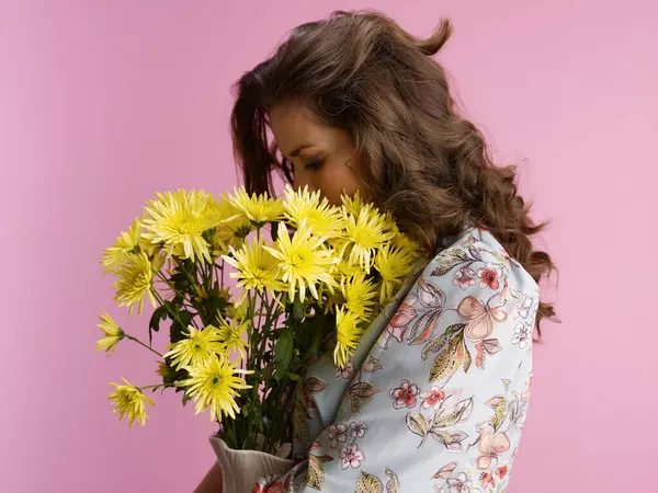 ピンクで隔離された花瓶の黄色い菊の花が付いている長い波のブルネットの髪のリラックスした若い女性 — ストック写真