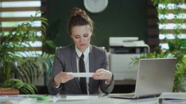 Yeni bir iş. Modern yeşil ofiste, gri takım elbiseli, laptoplu, düşünceli, modern kadın işçi..