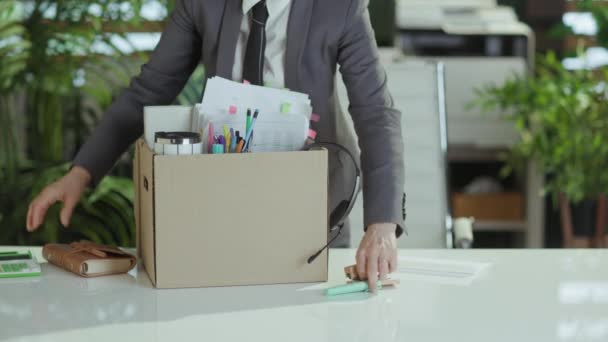 新しい仕事 現代の40歳の女性労働者をダンボール箱の個人的な持ち物が付いている灰色のビジネス スーツの現代緑のオフィスで閉めます — ストック動画